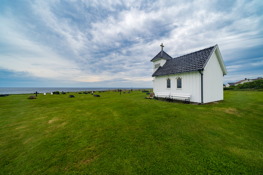 View of the small white Varhaug Old Cemetery chapel standing on a green lawn by the sea under a dramatic cloudy sky in Varhaug Rogaland Norway. View of the small white Varhaug Old Cemetery chapel standing on a green lawn by the sea under a dramatic cloudy sky in Varhaug Rogaland Norway.