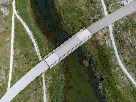 Aerial view of a bridge spanning a dark waterway contrasting with light pathways and grassy banks Duinvalleiweg Almere Flevoland Netherlands.