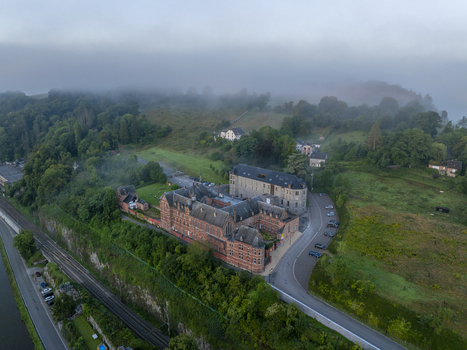 Aerial view of Maison Leffe surrounded by lush green hills trees a railway line and morning mist in Dinant Region wallonne Belgium.
