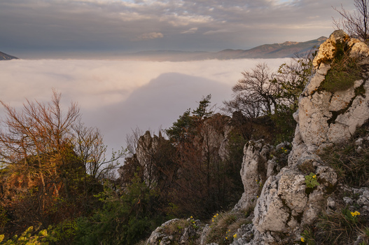 View of the rocky peak of Sip in Mala Fatra with limestone formations trees and a sea of clouds filling the valley below at sunset in Stankovany Zilina Region Slovakia. View of the rocky peak of Sip in Mala Fatra with limestone formations trees and a sea of clouds filling the valley below at sunset in Stankovany Zilina Region Slovakia.