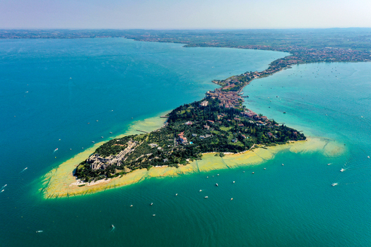 Aerial view of Grotte di Catullo e Museo Archeologico di Sirmione with ancient Roman ruins on the peninsula tip and turquoise waters of Lake Garda Sirmione Lombardia Italy. Aerial view of Grotte di Catullo e Museo Archeologico di Sirmione with ancient Roman ruins on the peninsula tip and turquoise waters of Lake Garda Sirmione Lombardia Italy.