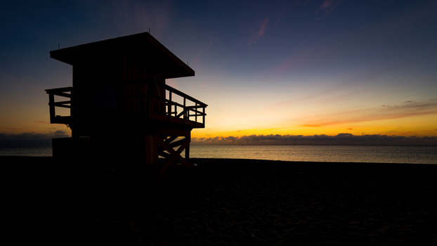 View of the silhouette of a lifeguard tower on the sandy beach during a vibrant sunrise over the ocean in Miami Beach Florida United States.