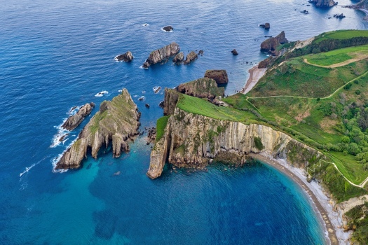 Aerial view of Silence Beach Viewpoint with dramatic vertical cliffs rocky islets in turquoise water and lush green hills Cudillero Asturias Spain.