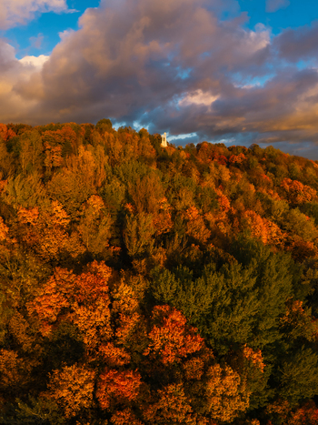 Aerial view of the vividly colored autumn foliage clinging to the hillside crowned by the stark white Three Crosses monument against a dramatic sky Vilnius Lithuania. Aerial view of the vividly colored autumn foliage clinging to the hillside crowned by the stark white Three Crosses monument against a dramatic sky Vilnius Lithuania.