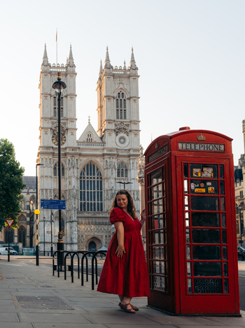 View of a woman in a bright red dress by a red phone booth with the grand white Westminster Abbey s detailed facade rising London England United Kingdom. View of a woman in a bright red dress by a red phone booth with the grand white Westminster Abbey s detailed facade rising London England United Kingdom.