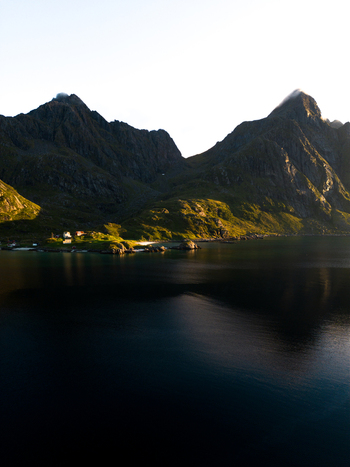 Aerial view of the coastal village of Tangstad nestled at the foot of dramatic steep mountains and calm dark waters during golden hour in Leknes Nordland Norway. Aerial view of the coastal village of Tangstad nestled at the foot of dramatic steep mountains and calm dark waters during golden hour in Leknes Nordland Norway.