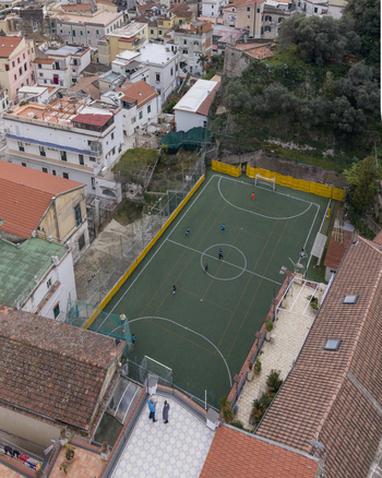Aerial view of a verdant football field nestled between rustic buildings with terracotta roofs and a lush green hillside Positano Campania Italy. Aerial view of a verdant football field nestled between rustic buildings with terracotta roofs and a lush green hillside Positano Campania Italy.