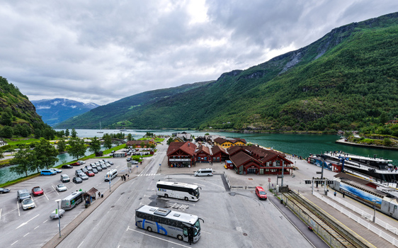 Aerial view of the village of Flam by the Aurlandsfjord featuring a parking area with buses a train station and surrounding green mountains under a cloudy sky in Flam Vestland Norway. Aerial view of the village of Flam by the Aurlandsfjord featuring a parking area with buses a train station and surrounding green mountains under a cloudy sky in Flam Vestland Norway.