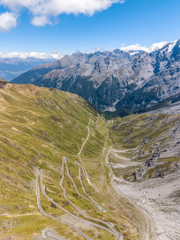 Aerial view of the iconic Stelvio Pass serpentines winding through the rugged alpine landscape of the Ortler Alps under a clear blue sky in Stilfs Trentino Alto Adige Italy.