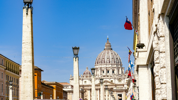View of St. Peter s Basilica seen from Via della Conciliazione with historic obelisks and flags under a clear blue sky in Rome Lazio Italy. View of St. Peter s Basilica seen from Via della Conciliazione with historic obelisks and flags under a clear blue sky in Rome Lazio Italy.