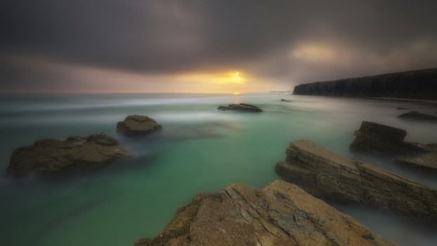 View of rocky coastline with turquoise water under a moody sunset sky in Galicia Spain. View of rocky coastline with turquoise water under a moody sunset sky in Galicia Spain.