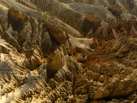 Aerial view of rugged eroded rocky canyons and dramatic arid landscape formations under bright sunlight in Nepal.