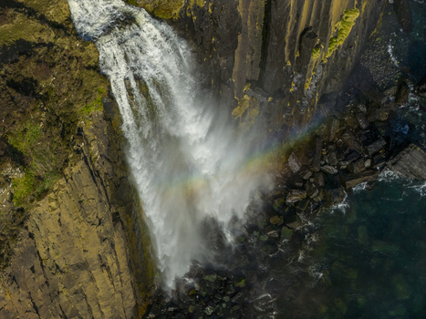 Aerial view of Mealt Falls plunging from Kilt Rock into the sea with a rainbow in the mist over basalt cliffs on the Isle of Skye Scotland United Kingdom. Aerial view of Mealt Falls plunging from Kilt Rock into the sea with a rainbow in the mist over basalt cliffs on the Isle of Skye Scotland United Kingdom.