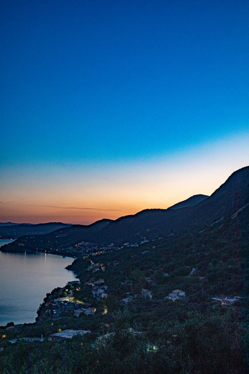 Aerial view of the coastline of Corfu at twilight with hills sloping down to the sea scattered lights from buildings and a gradient sky in Corfu Ionian Islands Greece. Aerial view of the coastline of Corfu at twilight with hills sloping down to the sea scattered lights from buildings and a gradient sky in Corfu Ionian Islands Greece.