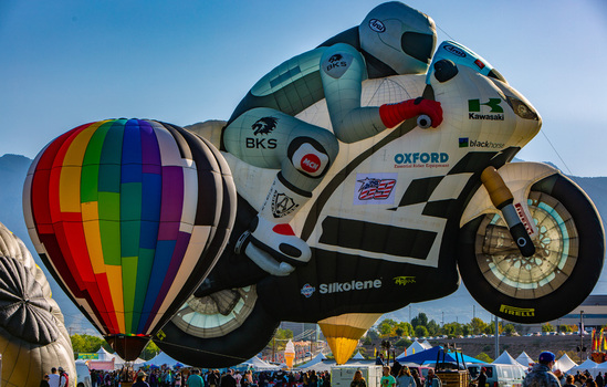 Albuquerque United States 09 October 2017 View of a motorcycle shaped balloon soaring above a vibrant crowd a rainbow balloon adding a splash of color against the distant mountains.