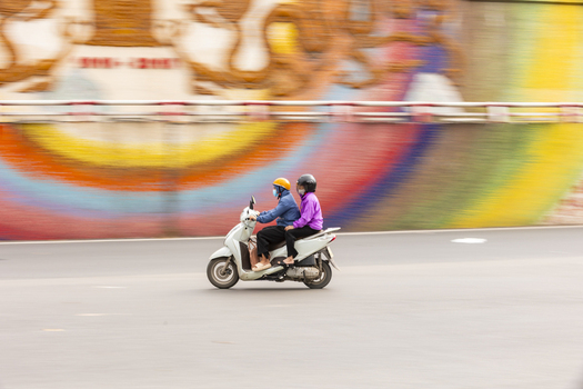 View of two people riding a scooter past the colorful Hanoi Ceramic Mosaic Mural in Hanoi Ha Noi Vietnam.
