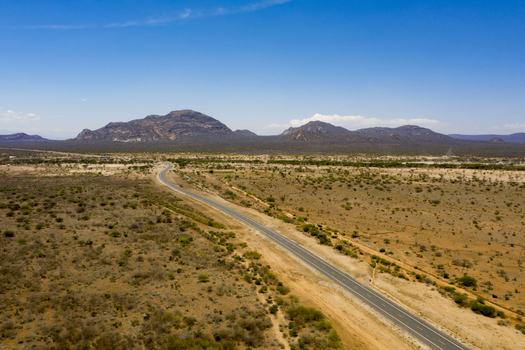 Aerial view of a paved road winding through the arid semi desert landscape of Marsabit County with distant mountains under a clear blue sky in Marsabit Marsabit County Kenya. Aerial view of a paved road winding through the arid semi desert landscape of Marsabit County with distant mountains under a clear blue sky in Marsabit Marsabit County Kenya.