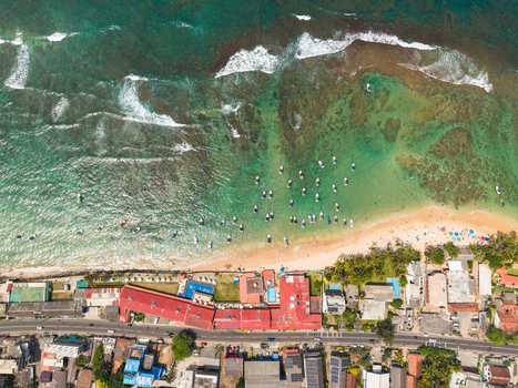 Aerial view of the turquoise coastline with small boats anchored near the sandy beach and red roofed buildings along the road in Hikkaduwa Southern Province Sri Lanka. Aerial view of the turquoise coastline with small boats anchored near the sandy beach and red roofed buildings along the road in Hikkaduwa Southern Province Sri Lanka.