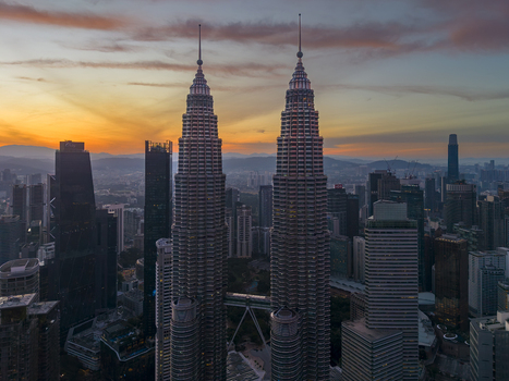 Kuala Lumpur Malaysia 11 March 2026 Aerial view of the Petronas Twin Towers towering over the city skyline during a vibrant sunset with orange and purple clouds.