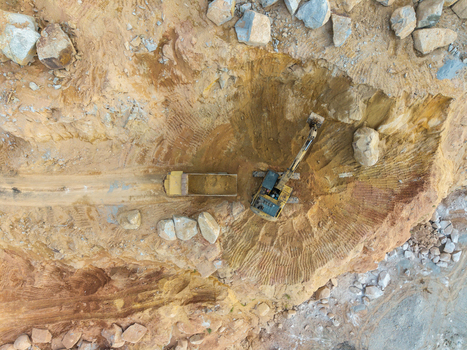 Aerial view of an active mining site featuring an excavator loading earth into a dump truck amidst rocky terrain and excavated soil in Bukit Tambun Penang Malaysia. Aerial view of an active mining site featuring an excavator loading earth into a dump truck amidst rocky terrain and excavated soil in Bukit Tambun Penang Malaysia.