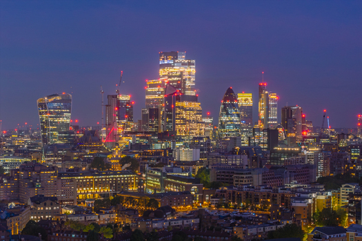 Aerial view of the illuminated City of London skyline at dusk featuring iconic skyscrapers rising above the dense urban landscape of London England United Kingdom.
