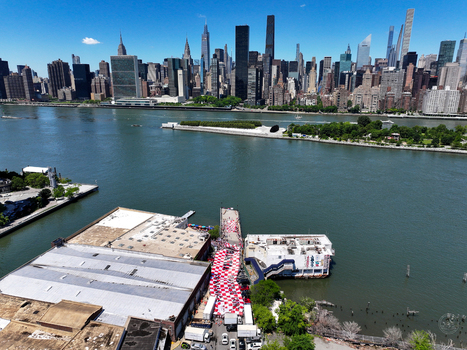 Long Island City United States 13 June 2026 Aerial view of a large red and white checkered banner on a pier along the East River with the Manhattan skyline in the background.