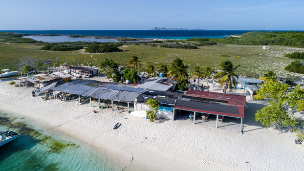 Aerial view of Los Roques archipelago featuring rustic coastal structures small boats on white sand beaches and palm trees in Los Roques Dependencias Federales Venezuela. Aerial view of Los Roques archipelago featuring rustic coastal structures small boats on white sand beaches and palm trees in Los Roques Dependencias Federales Venezuela.