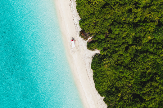 Aerial view of a lush tropical island with tall palm trees and dense vegetation surrounded by crystal clear turquoise lagoon water Innafinolhu Haa Alif Atoll Maldives. Aerial view of a lush tropical island with tall palm trees and dense vegetation surrounded by crystal clear turquoise lagoon water Innafinolhu Haa Alif Atoll Maldives.