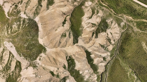 Aerial view of sun baked earth reveals a tapestry of textures and tones where arid land meets sporadic hints of green Centuripe Sicilia Italy.