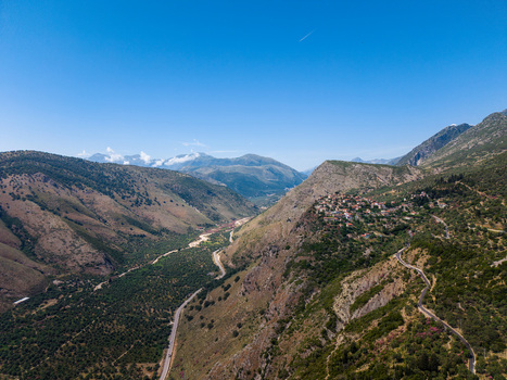 Aerial view of the historic village of Qeparo Fshat on a mountain slope overlooking a lush green valley and winding road under a clear blue sky in Qeparo Fshat Vlore County Albania. Aerial view of the historic village of Qeparo Fshat on a mountain slope overlooking a lush green valley and winding road under a clear blue sky in Qeparo Fshat Vlore County Albania.