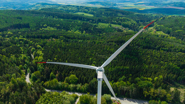 Aerial view of Zipotin wind turbine standing tall amidst a lush green forest and rolling hills under a clear sky Gruna Pardubicky kraj Czechia. Aerial view of Zipotin wind turbine standing tall amidst a lush green forest and rolling hills under a clear sky Gruna Pardubicky kraj Czechia.