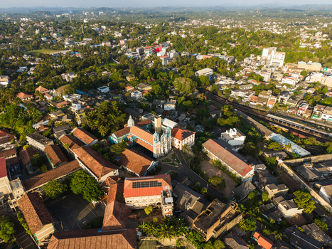 Aerial view of St. Mary s Cathedral surrounded by red roofed buildings and lush tropical greenery under golden sunlight in Galle Southern Province Sri Lanka.