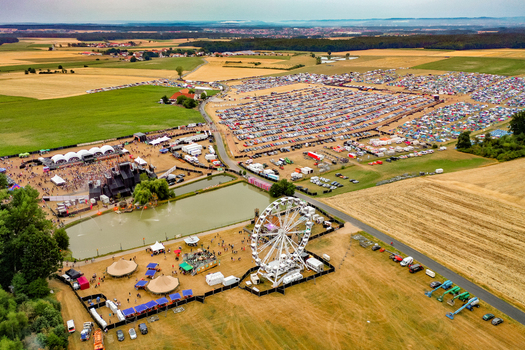 Herzogenaurach Germany 22 July 2022 Aerial view of the Open Beatz Festival featuring a Ferris wheel large stages and a massive parking area surrounded by rural fields. Herzogenaurach Germany 22 July 2022 Aerial view of the Open Beatz Festival featuring a Ferris wheel large stages and a massive parking area surrounded by rural fields.