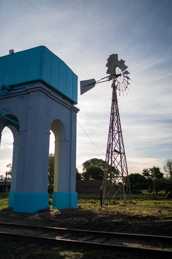 View of a blue water tower and a metal windmill standing in a rural field near railway tracks in Guaviravi Corrientes Province Argentina.