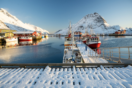 Nordland Norway 21 September 2026 View of fishing boats docked in a snowy harbor in Lofoten surrounded by snow capped mountains under a clear blue sky. Nordland Norway 21 September 2026 View of fishing boats docked in a snowy harbor in Lofoten surrounded by snow capped mountains under a clear blue sky.