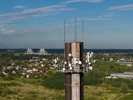 Aerial view of a telecommunications tower with multiple antennas set against a rural landscape with a bridge in the distance in Poland. Aerial view of a telecommunications tower with multiple antennas set against a rural landscape with a bridge in the distance in Poland.