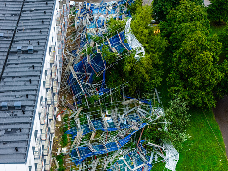 Riga Latvia 23 August 2026 Aerial view of collapsed construction scaffolding against a building facade with twisted metal frames and blue safety netting scattered among trees.