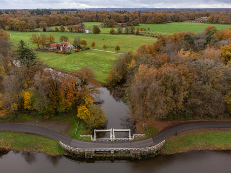 Aerial view of a winding road and bridge over calm waters reflecting the autumn trees with a distant farmhouse Schuivenhuisje Overijssel Netherlands. Aerial view of a winding road and bridge over calm waters reflecting the autumn trees with a distant farmhouse Schuivenhuisje Overijssel Netherlands.