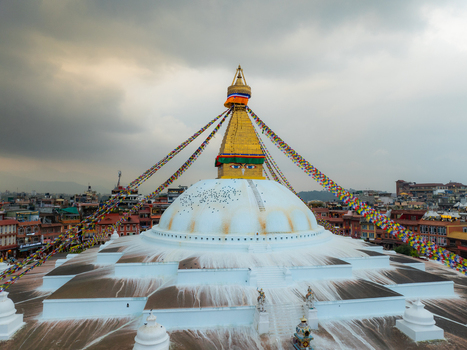 Aerial view of the Boudhanath Stupa with its iconic golden spire and colorful prayer flags surrounded by the urban landscape of Kathmandu Nepal.