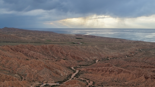 Aerial view of red sandstone rock formations at Jety Oguz with a winding dirt road dramatic storm clouds and Issyk Kul lake in the distance in Jety Oguz Issyk Kul Region Kyrgyzstan. Aerial view of red sandstone rock formations at Jety Oguz with a winding dirt road dramatic storm clouds and Issyk Kul lake in the distance in Jety Oguz Issyk Kul Region Kyrgyzstan.