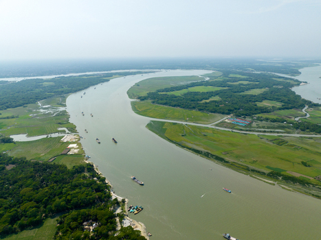 Aerial view of a wide river snaking through lush greenery with boats dotting its surface under a soft sky Charmonai Barisal Division Bangladesh. Aerial view of a wide river snaking through lush greenery with boats dotting its surface under a soft sky Charmonai Barisal Division Bangladesh.