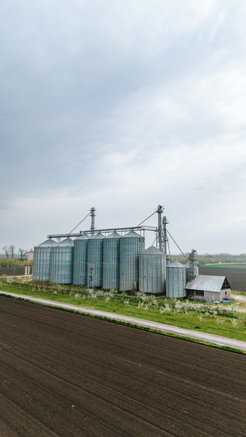 Aerial view of the towering silver grain elevators standing guard over the dark tilled earth under a vast muted sky Sremska Mitrovica Vojvodina Serbia. Aerial view of the towering silver grain elevators standing guard over the dark tilled earth under a vast muted sky Sremska Mitrovica Vojvodina Serbia.