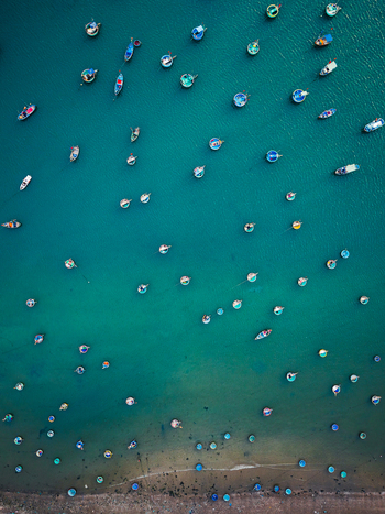 Aerial view of numerous traditional round basket boats scattered across the vibrant turquoise water near the sandy coastline of Vietnam. Aerial view of numerous traditional round basket boats scattered across the vibrant turquoise water near the sandy coastline of Vietnam.