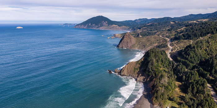 Aerial view of the rugged southern oregon coast featuring dramatic cliffs forested hills and the winding coastal highway meeting the pacific ocean in Port Orford Oregon United States. Aerial view of the rugged southern oregon coast featuring dramatic cliffs forested hills and the winding coastal highway meeting the pacific ocean in Port Orford Oregon United States.