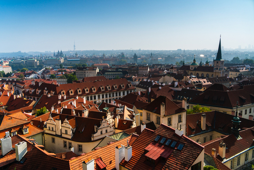 View of the historic red tiled rooftops of Prague featuring traditional architecture chimneys and church spires under a clear blue sky in Prague Prague Czechia.