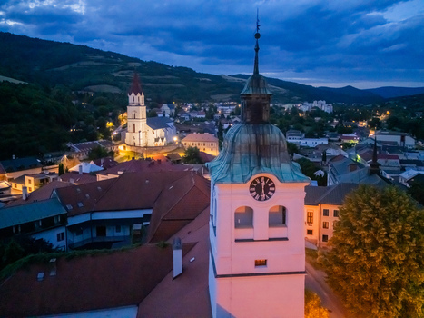 Aerial view of the illuminated clock tower and spire of a church rise amidst the rooftops of a tranquil town nestled beneath shadowy mountains Gelnica Kosice Region Slovakia. Aerial view of the illuminated clock tower and spire of a church rise amidst the rooftops of a tranquil town nestled beneath shadowy mountains Gelnica Kosice Region Slovakia.