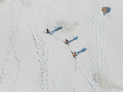 Aerial view of three skiers trekking across the snowy slopes of Versante sud dell Etna with long shadows and tracks on the white surface Nicolosi Sicilia Italy. Aerial view of three skiers trekking across the snowy slopes of Versante sud dell Etna with long shadows and tracks on the white surface Nicolosi Sicilia Italy.
