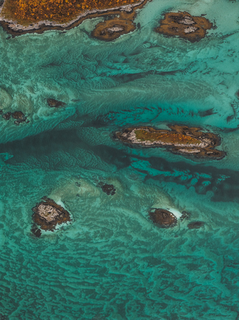 Aerial view of the turquoise waters surrounding the rocky islands of Senja showcasing clear shallow sea patterns and rugged coastal terrain in Senja Troms Norway.