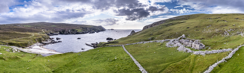 Aerial view of the historic ruins of An Port featuring stone walls and cottages nestled among green hills overlooking a secluded beach in Ardara County Donegal Ireland.