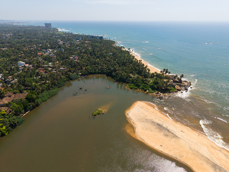 Aerial view of a river mouth meeting the Indian Ocean with a sandy beach and lush palm trees in Galle Southern Province Sri Lanka.